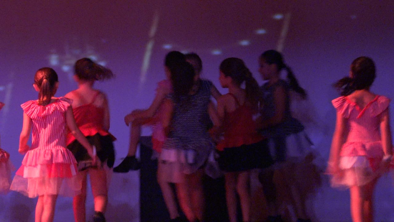 Group of girls in dance costumes clustered near center stage.