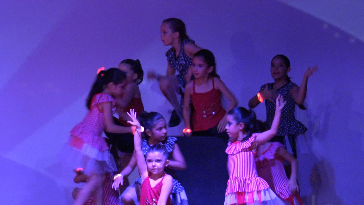 Children perform on a purple-lit stage in San Jose del Cabo BCS Mexico, with several dancers clustered at left and front performers raising their arms.
