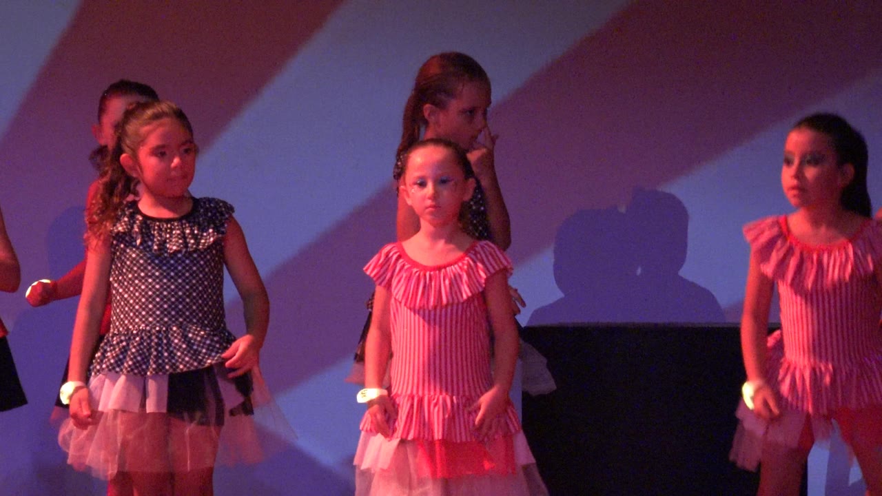Children dancing on stage, with one girl bending forward and others standing behind her.