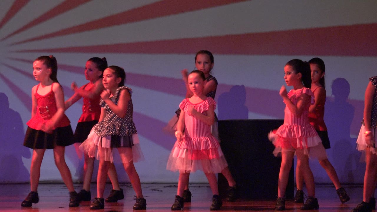 Children in dance costumes hold poses across a stage.