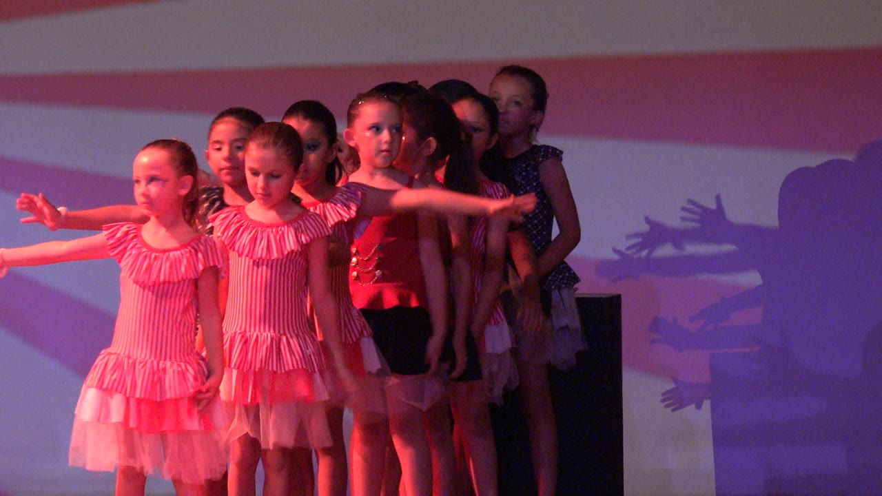 Children dancers extend their arms in a synchronized stage formation.