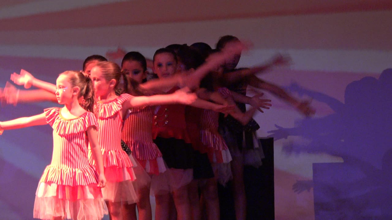 Two girls in pink dresses lead the front of the formation in San Jose del Cabo BCS Mexico while more young dancers move behind them under pink and purple stage light.
