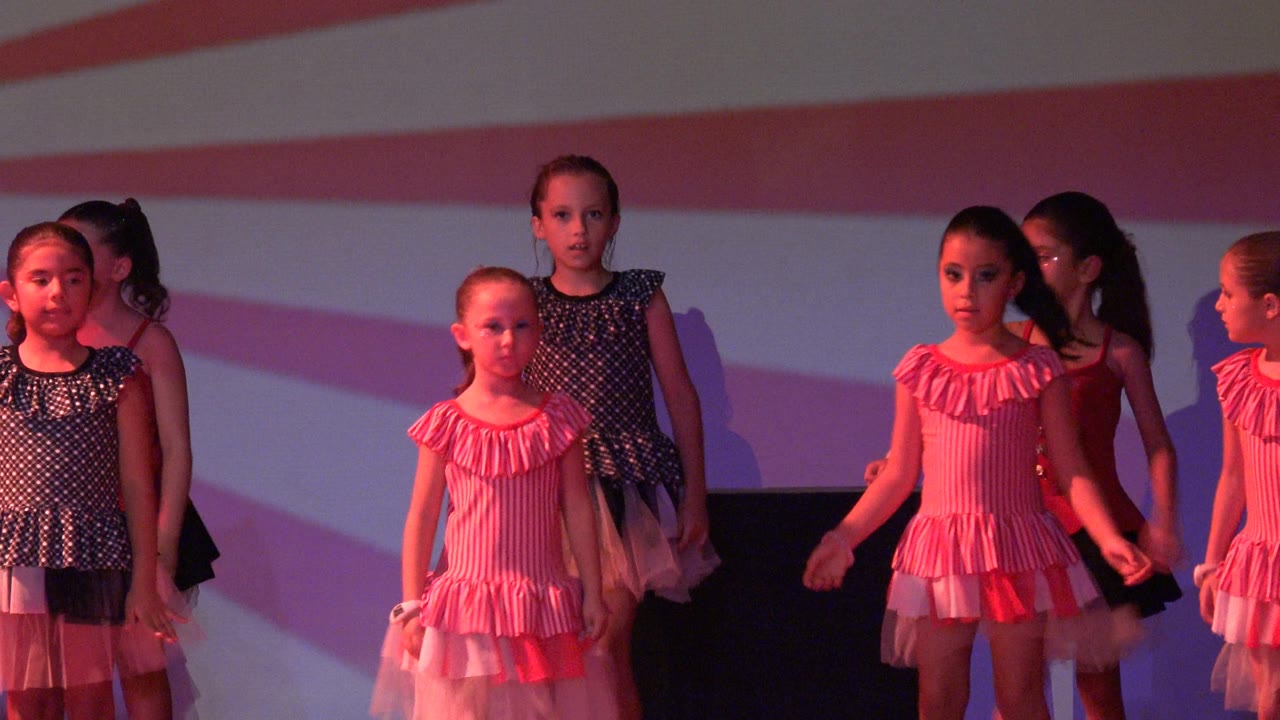 Girls face forward on stage as the formation shifts.