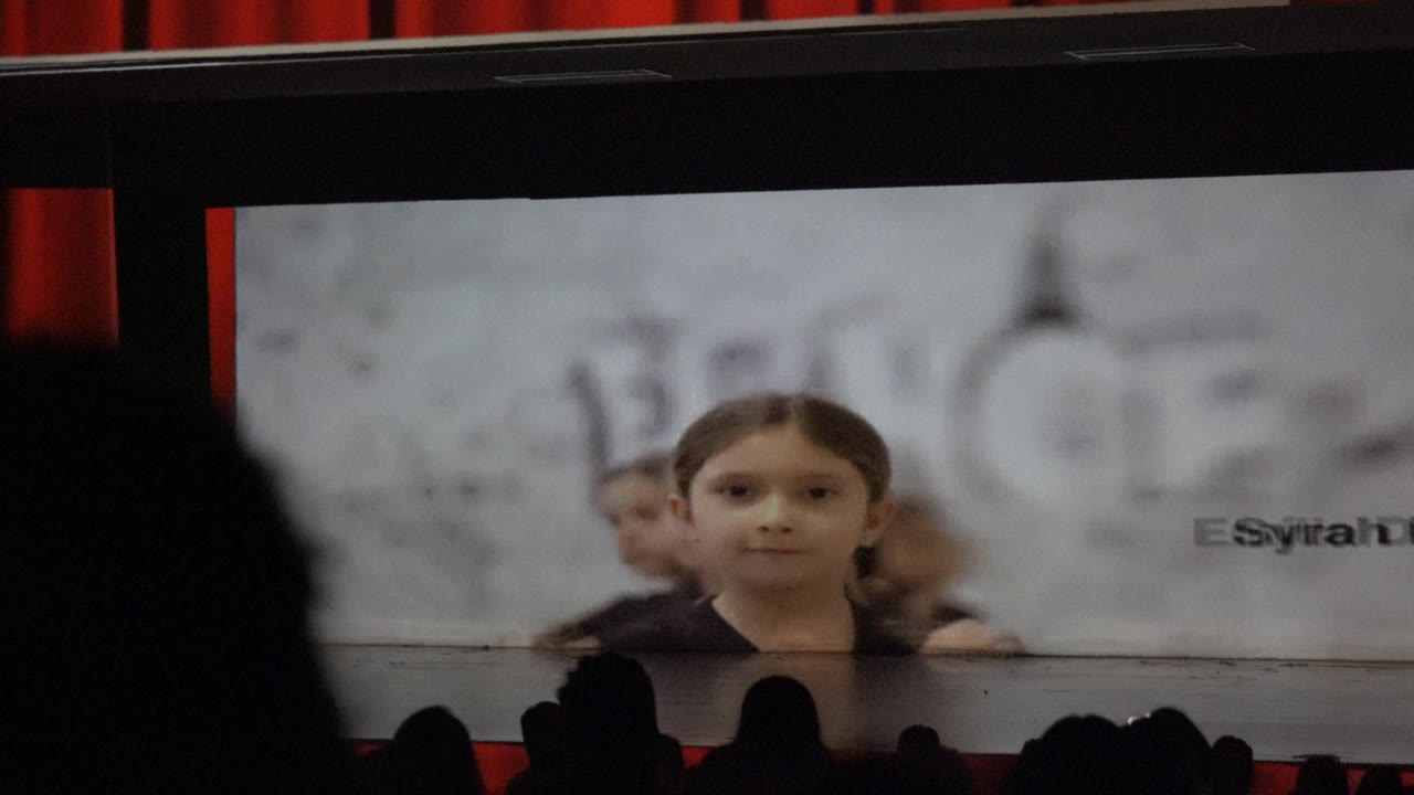 In San Jose Del Cabo BCS Mexico, a girl appears centered on a large projection screen while dark audience silhouettes line the bottom of the frame.