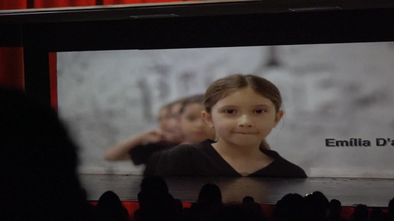 Projected portrait of a girl with name text beside her and audience silhouettes in front.