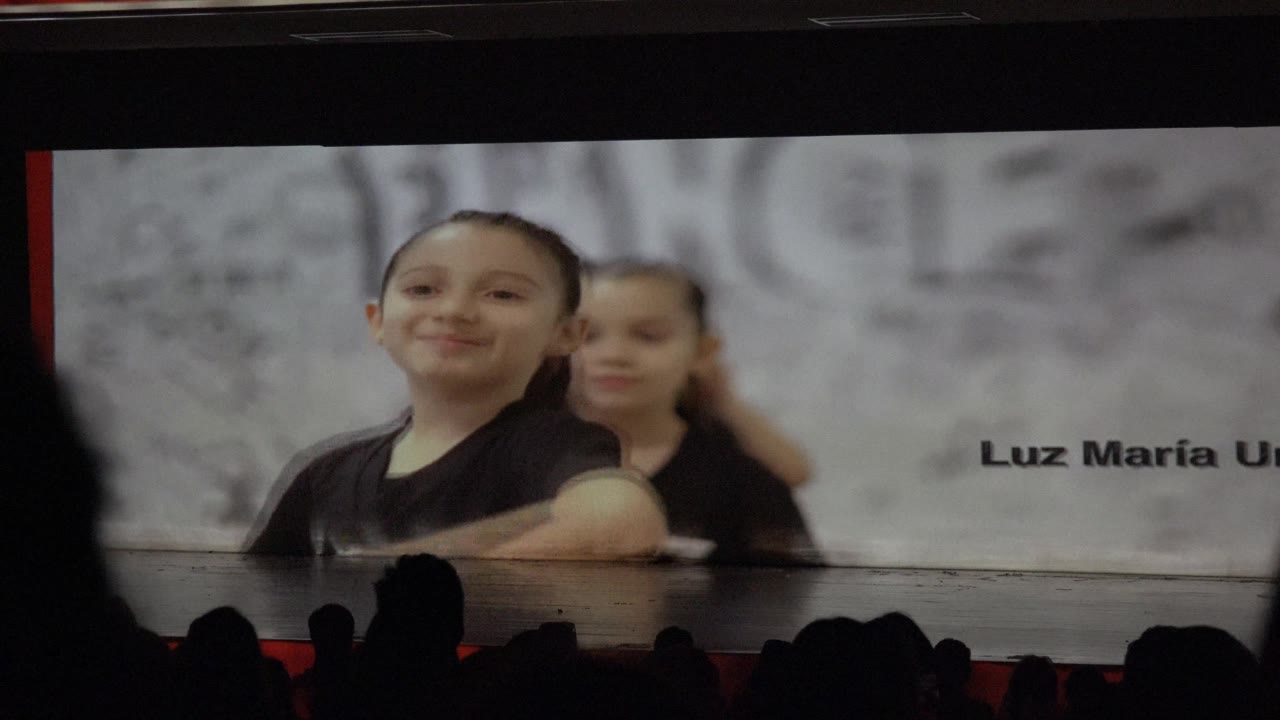 Smiling child performer centered in front of another child and a projected name.