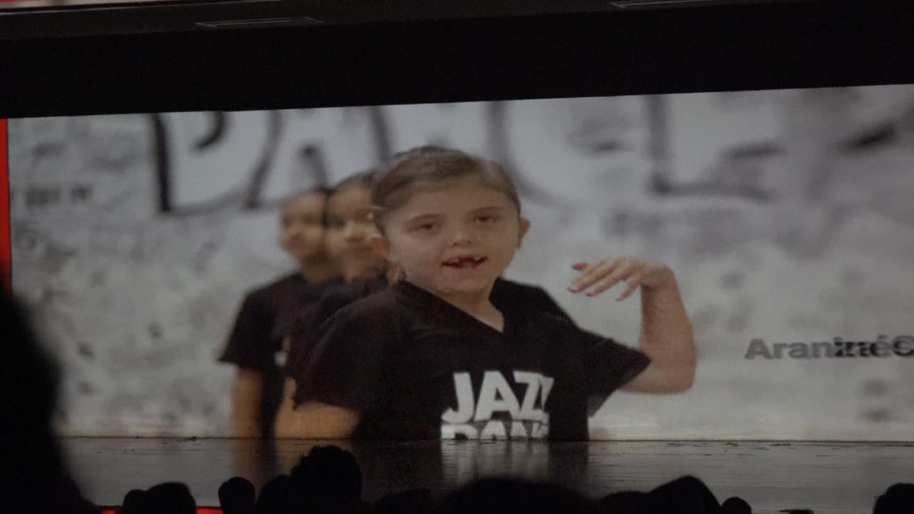 Girl in black Jazz Dance shirt raises one hand while other children line up behind her.