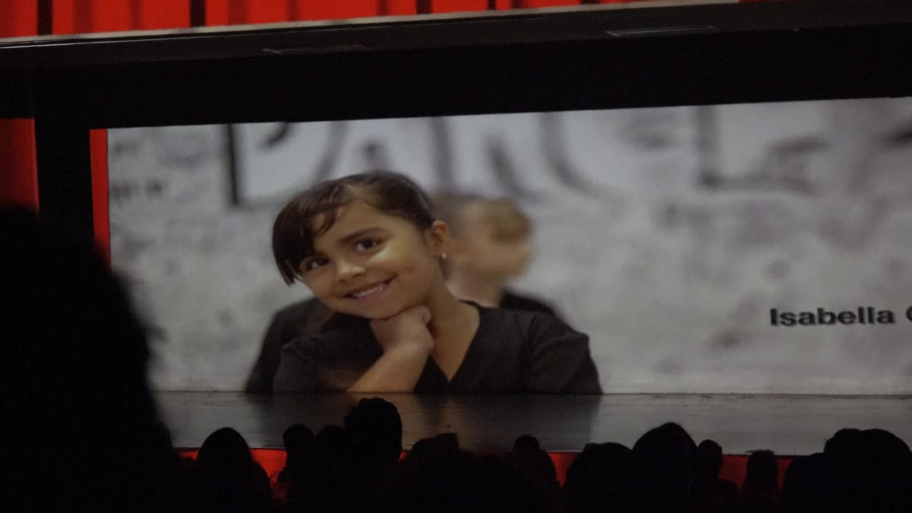 In San Jose Del Cabo BCS Mexico 2023 footage, a child smiles on a large stage screen while audience silhouettes sit across the bottom of the frame.