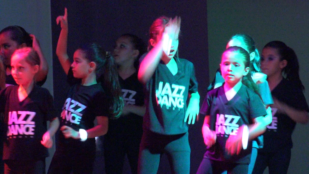 Children in matching Jazz Dance shirts move through the routine in San Jose Del Cabo, Mexico, with one dancer turned in profile and green light on the front row.