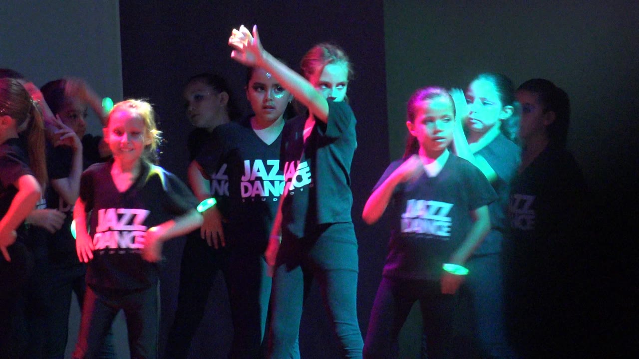 Children in black Jazz Dance shirts perform on an indoor stage in San Jose del Cabo BCS Mexico, with one dancer raising an arm as purple and green light crosses the group.
