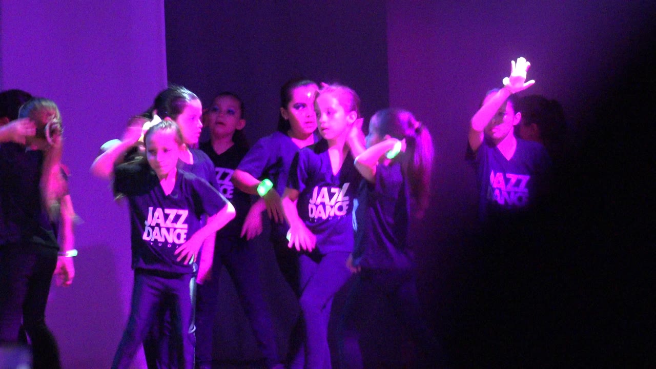 Dance group clustered on stage in purple lighting.