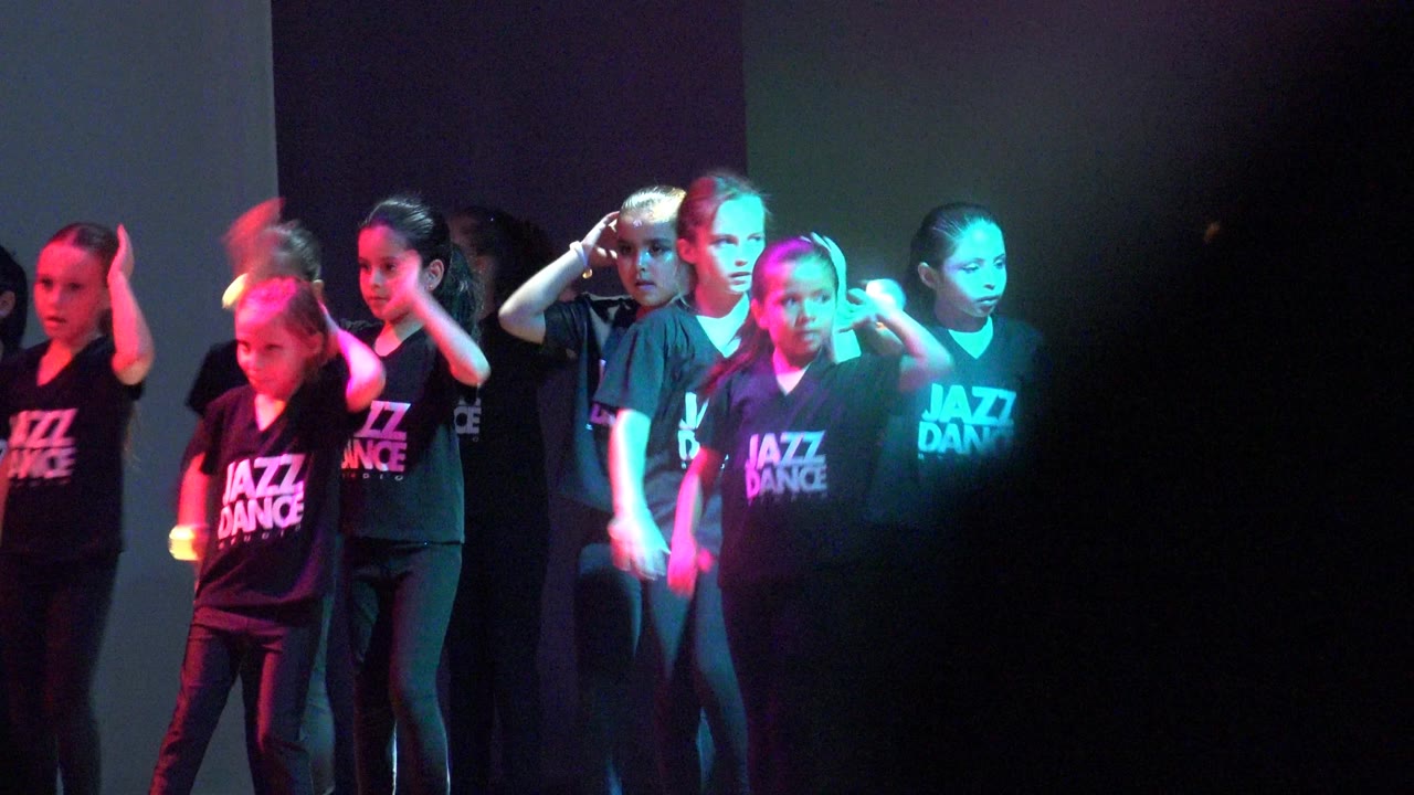 Children in black Jazz Dance shirts gather on a stage in San Jose del Cabo BCS Mexico, with purple and teal lighting and audience silhouettes at the bottom edge.