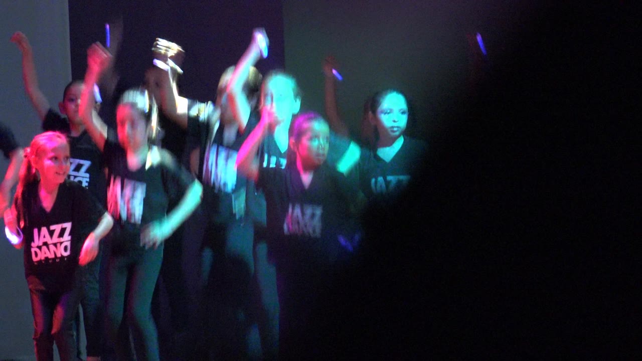 Children continue the jazz routine in San Jose del Cabo BCS Mexico, with one central dancer blurred by fast movement and others lit by teal and purple stage light.