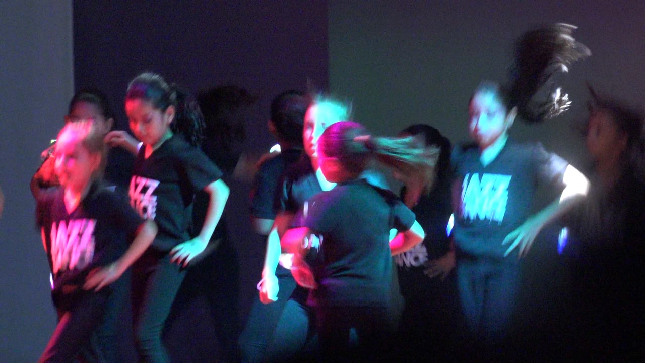 Children in black Jazz Dance shirts perform on a dark stage in San Jose del Cabo BCS Mexico, with magenta and cyan light and visible motion blur from fast movement.