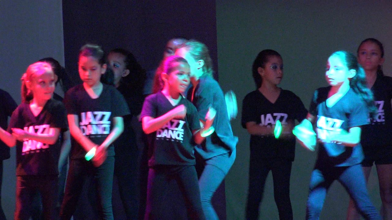 Children in black Jazz Dance shirts stand and move on a stage in San Jose del Cabo BCS Mexico, with red and green light falling across the group.