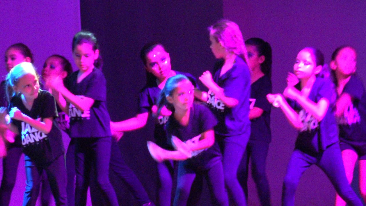 Children perform a dance move under strong purple stage lighting.