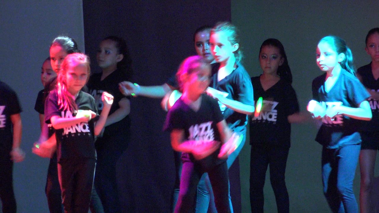 Several children in black Jazz Dance shirts continue the routine in San Jose del Cabo BCS Mexico, with cyan and red lighting crossing their faces and shirts.