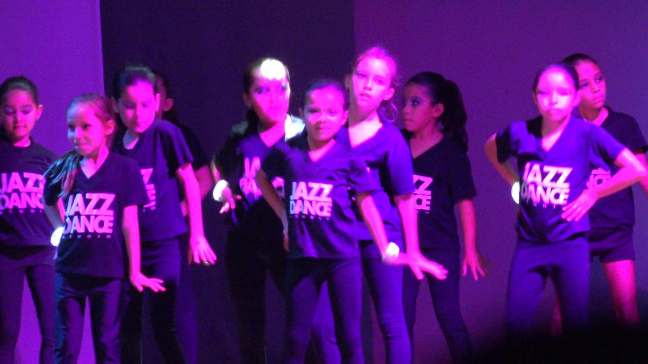 Children dancing in matching shirts under purple stage lights.