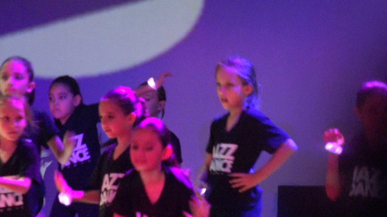Children perform in black Jazz Dance shirts on a purple-lit stage in San Jose del Cabo, Mexico, with one dancer standing near the right and others grouped at left.