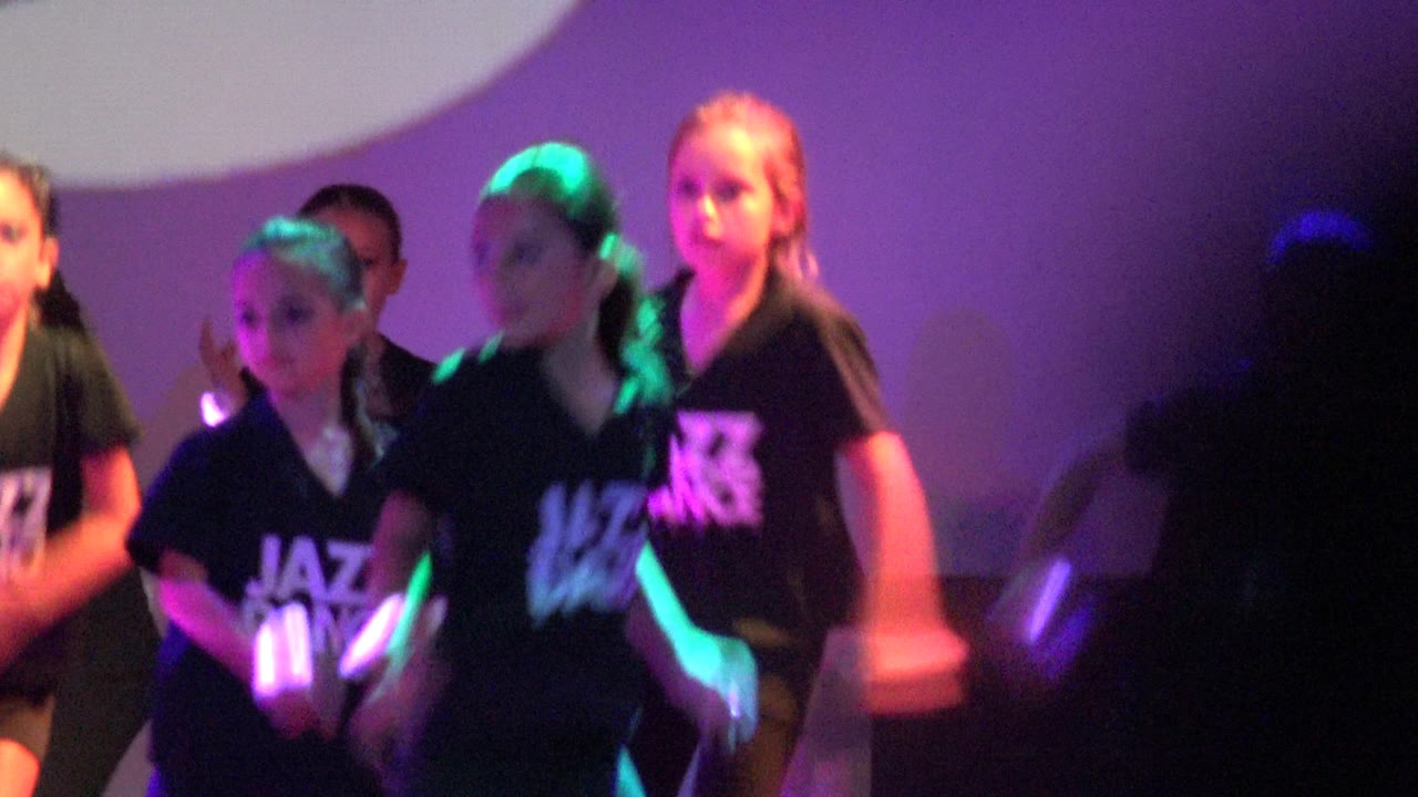 Children in black shirts face forward during a jazz dance routine.
