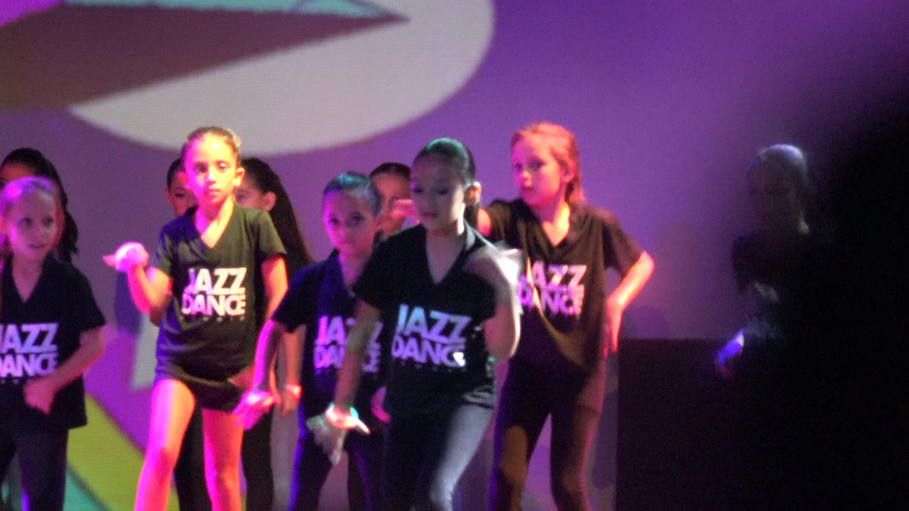 Children dancing in formation with colored lights on a stage.