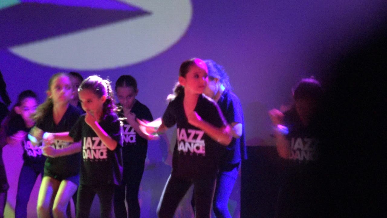 Young dancers perform on a purple-lit stage in San Jose Del Cabo BCS Mexico, with several faces visible and a white projection shape behind them.
