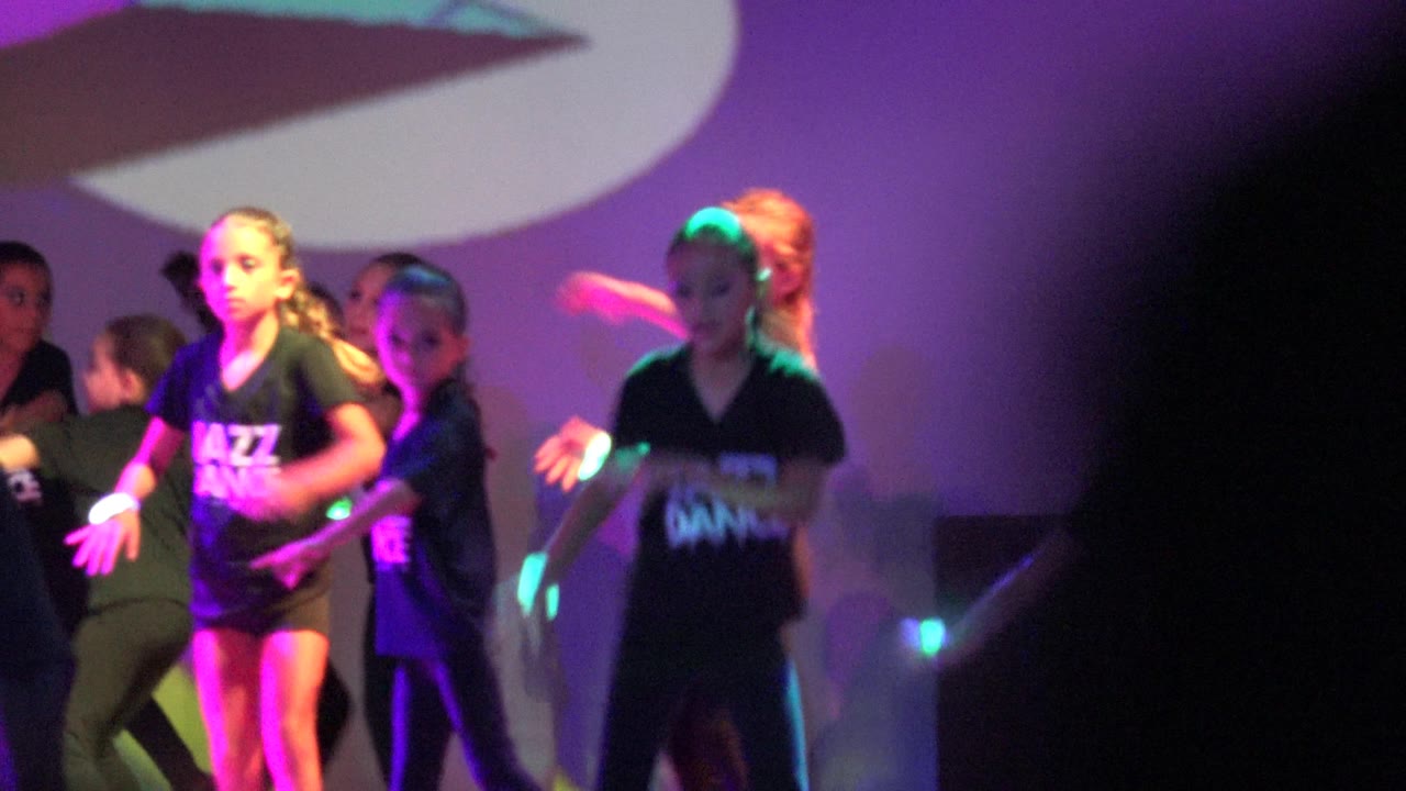 A child dancer stands near center as other children move behind her.
