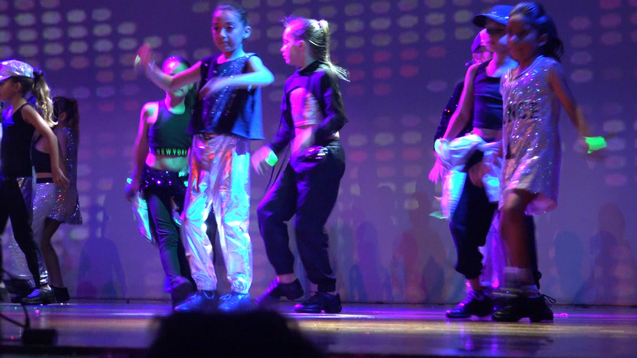Children in shiny and black outfits crossing the stage.
