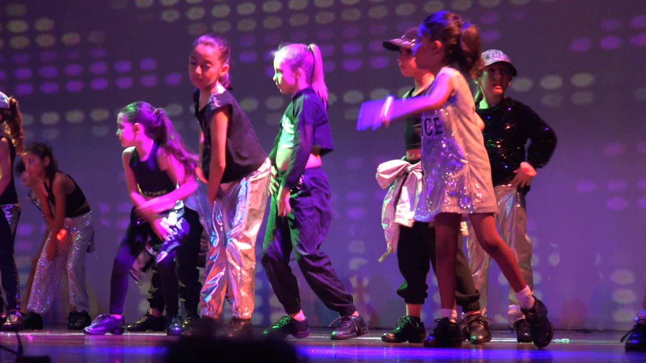 Children perform on a San Jose del Cabo BCS Mexico stage under purple and green lighting, with silver and black outfits visible across the group.
