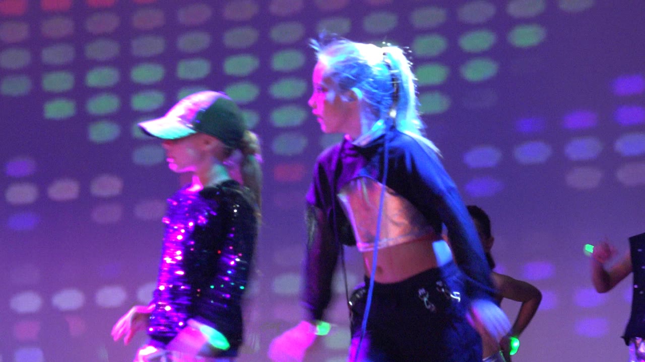 Two dancers cross under purple and blue stage lights.