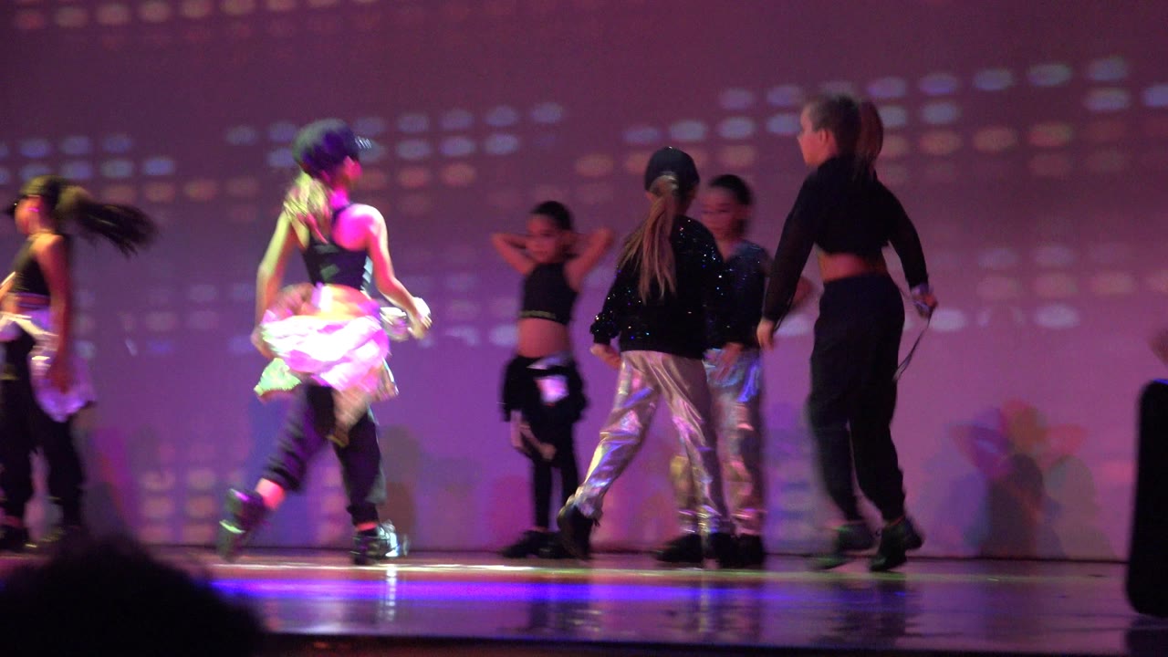 Children perform on a purple-lit stage in San Jose Del Cabo BCS Mexico, with one dancer crossing at left and others in black and silver costumes near the center.