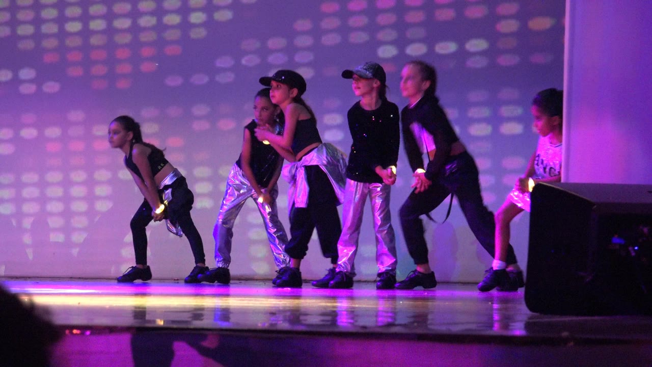 Children lean forward and step together during a stage dance routine.