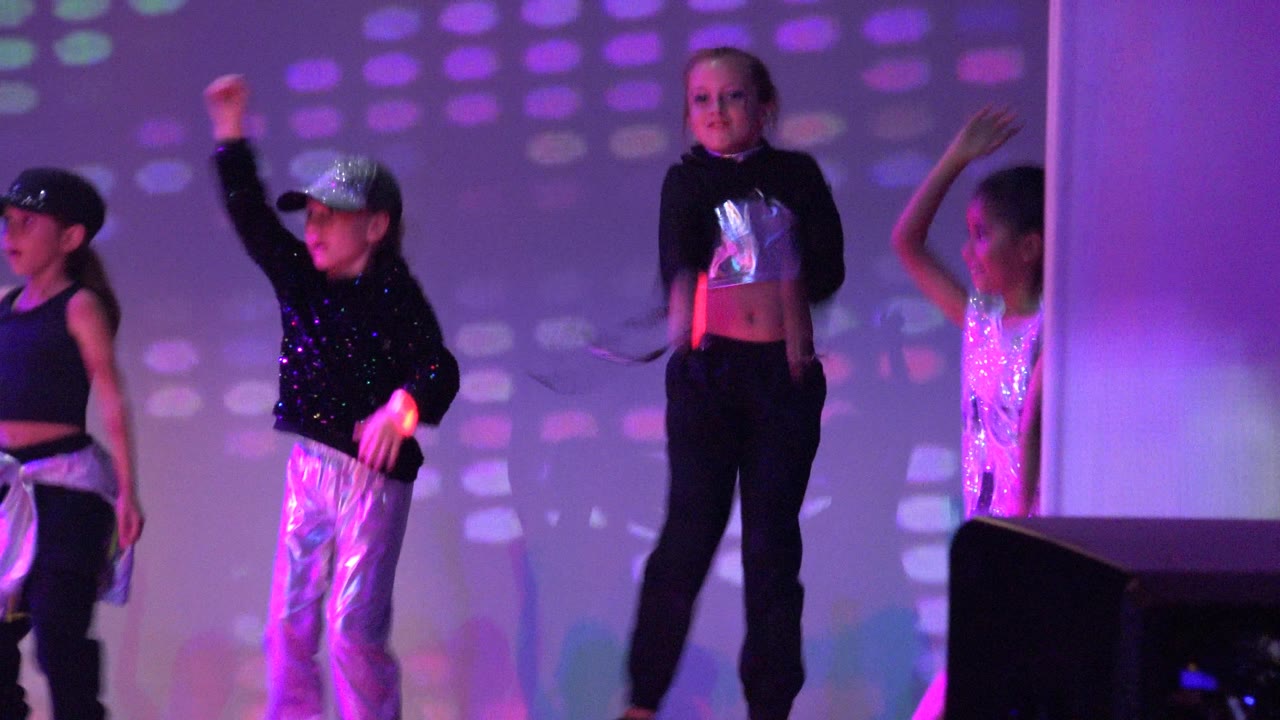 Children raising arms during a synchronized dance routine under colored lights.