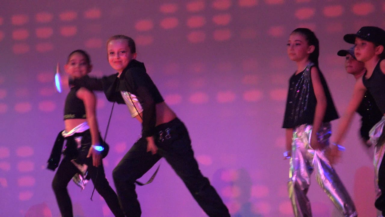 Children perform a choreographed dance on a purple and pink lit stage in San Jose Del Cabo BCS Mexico, with one dancer leaning forward while others stand nearby.