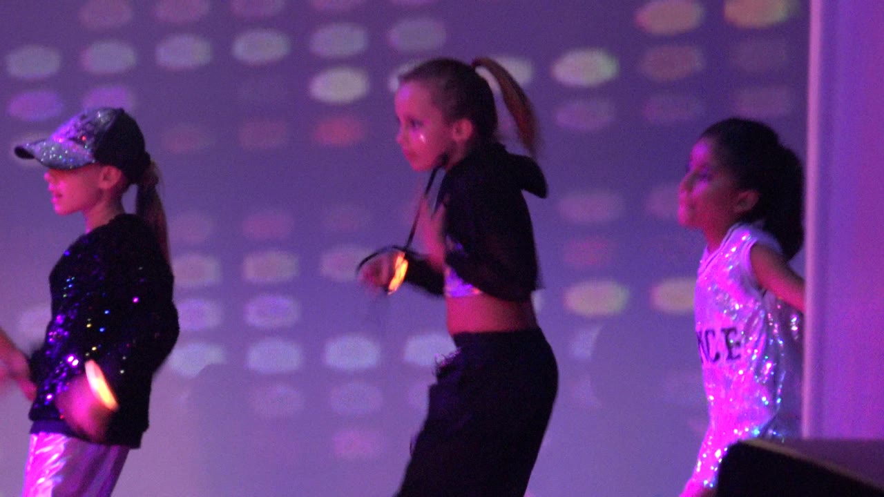 Three children mid-dance under purple stage lights.