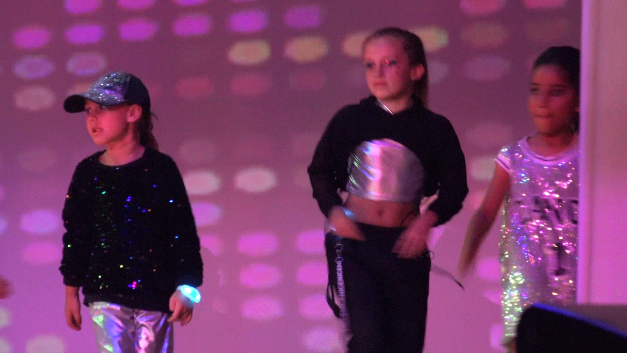 Children stand and move through a choreographed moment on a pink and purple stage in San Jose del Cabo BCS Mexico, with silver costumes catching the colored light.