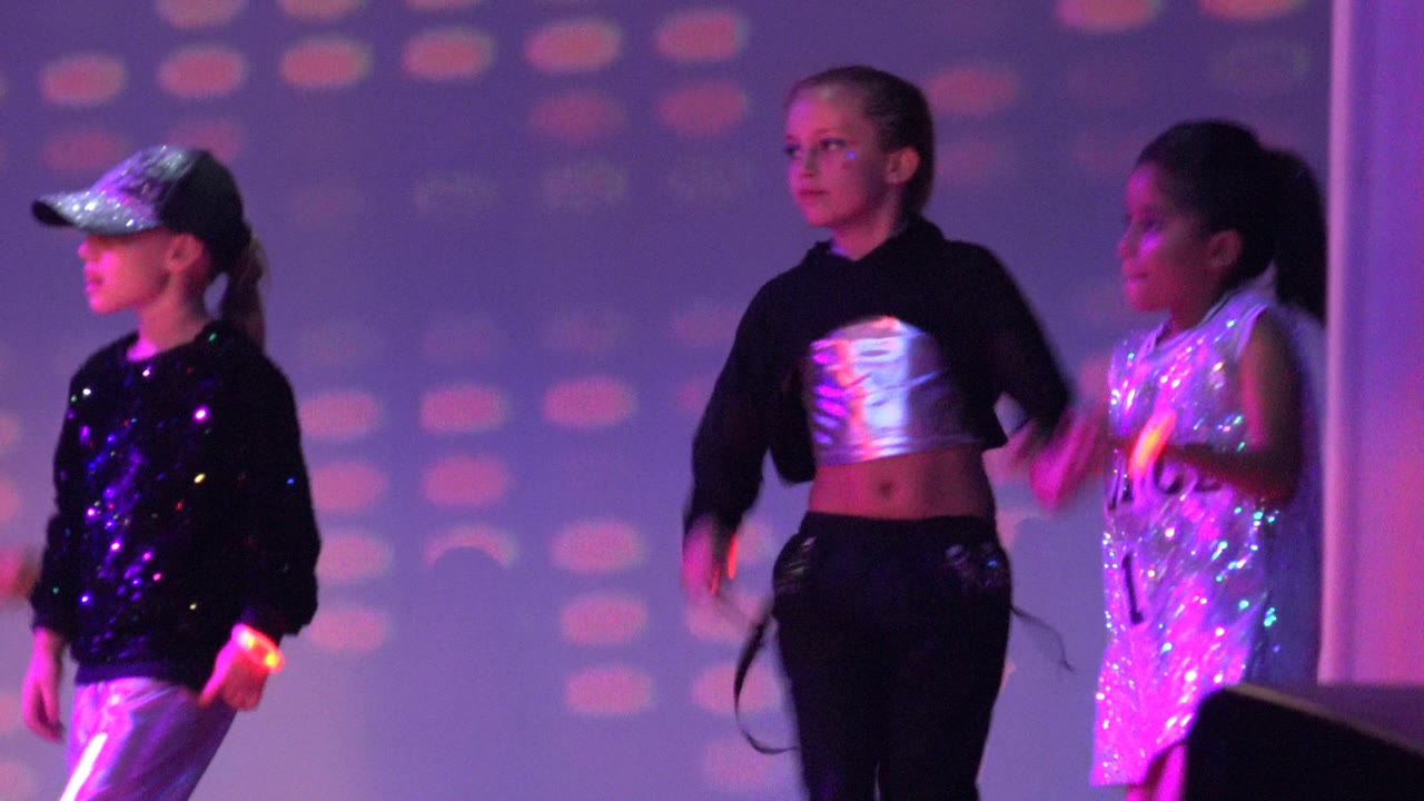 Three children onstage with a dark monitor in the foreground.
