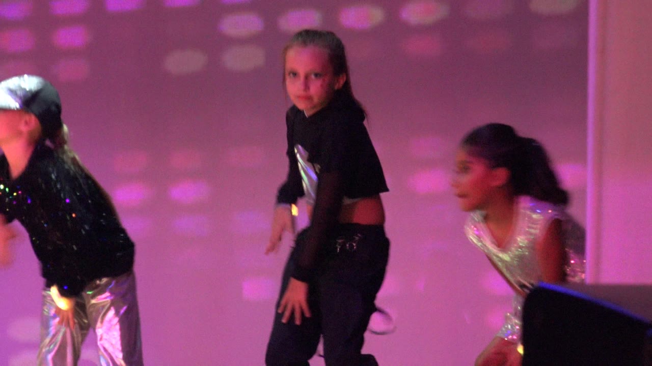 Children perform on a purple-lit stage in San Jose Del Cabo BCS Mexico, with one child in a black crop top centered and other dancers partly visible at the edges.