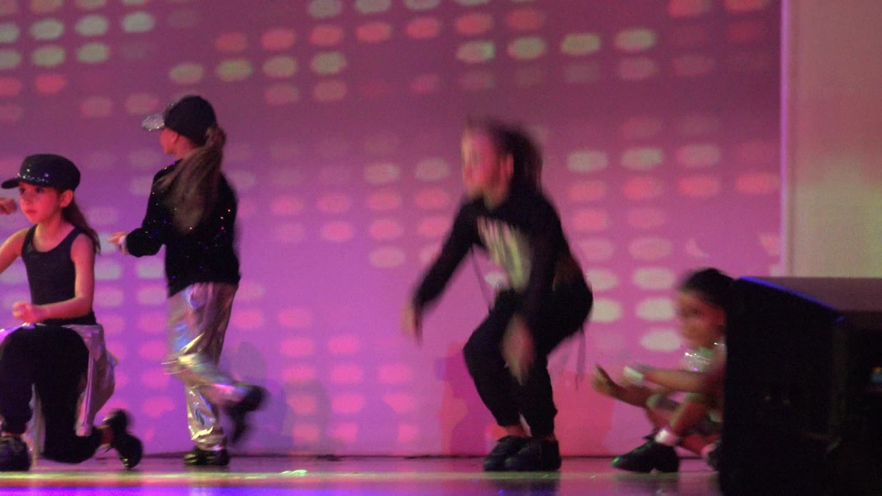Children perform on a stage in San Jose Del Cabo BCS Mexico, with one dancer blurred mid-move and others kneeling under pink and purple light.