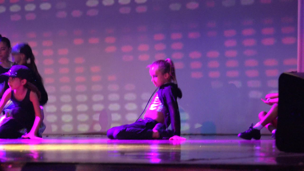 Children seated and kneeling on a purple lit stage