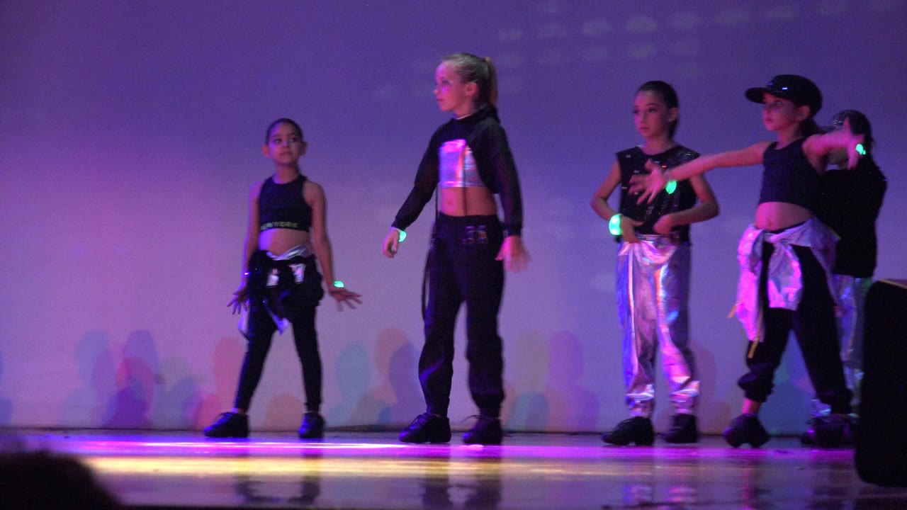 Children dancers spaced across a stage with purple lighting.