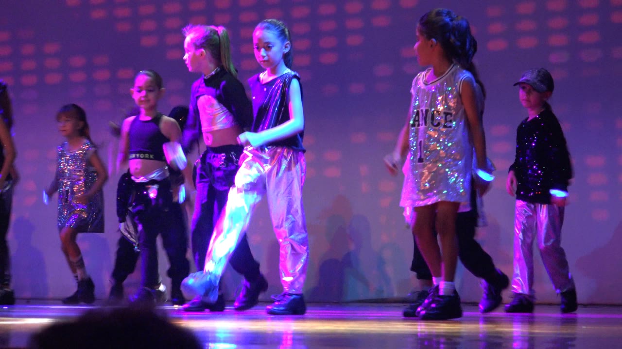 Children step in formation under magenta and blue stage lights.