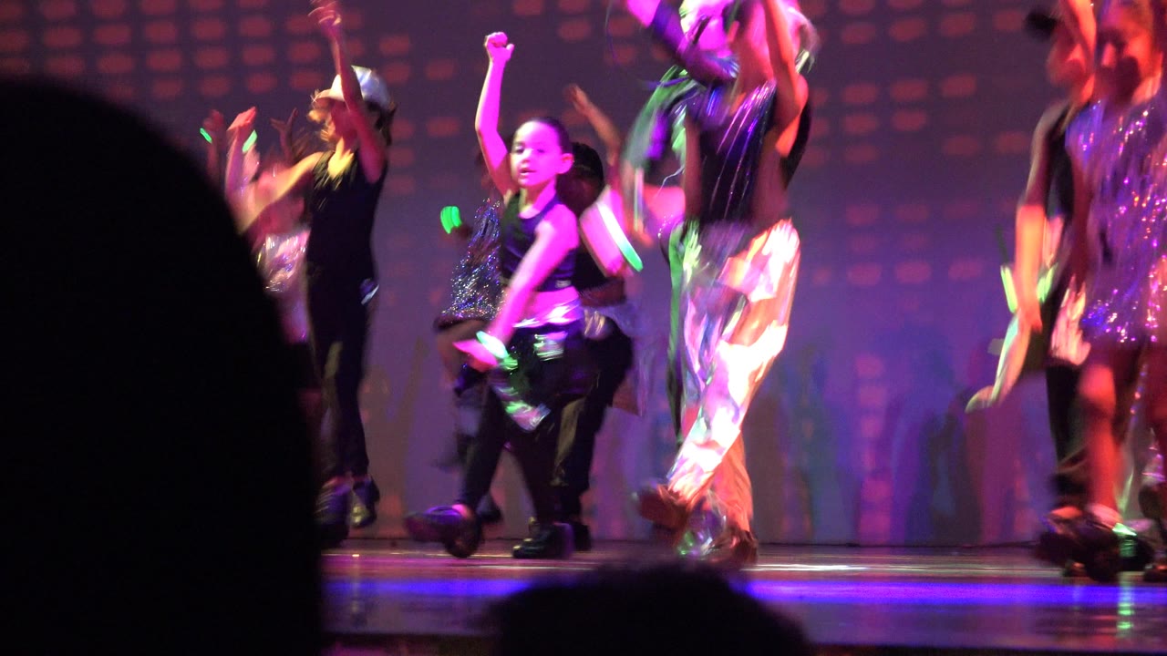 Young dancers perform on a San Jose Del Cabo BCS Mexico stage under magenta and blue lighting, with dark audience silhouettes cutting into the foreground.