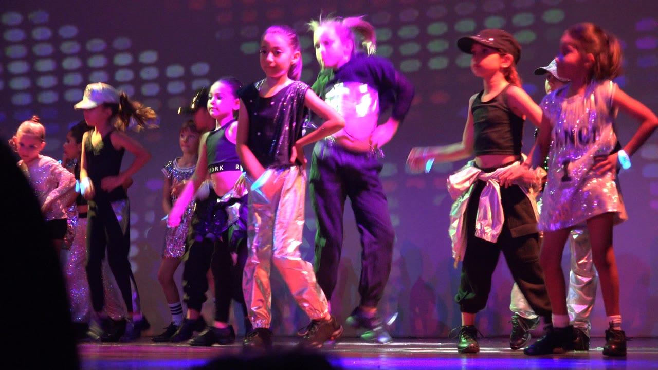 Children perform on a stage in San Jose Del Cabo BCS Mexico, with several dancers facing forward under purple and pink lights.