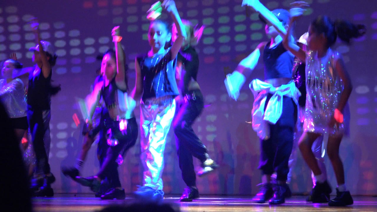 Children raise arms and step during a stage dance routine.
