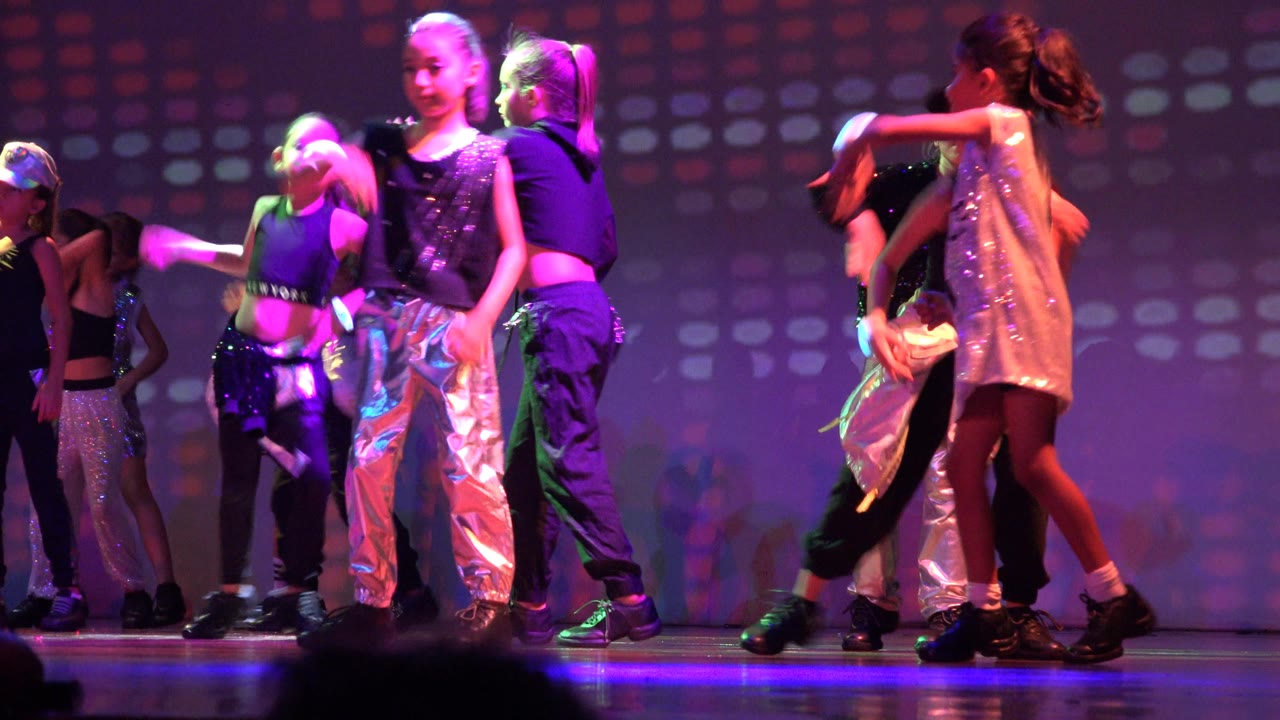 A children's dance ensemble performs in San Jose Del Cabo BCS Mexico, with a front dancer in shiny silver pants and others grouped behind under purple stage light.