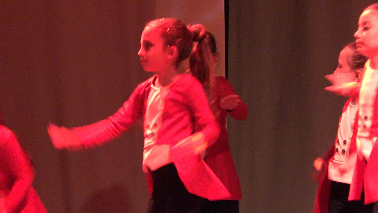 A girl in a red jacket and white top dances on a red-lit stage in San Jose Del Cabo BCS Mexico, with another performer partly hidden behind her.
