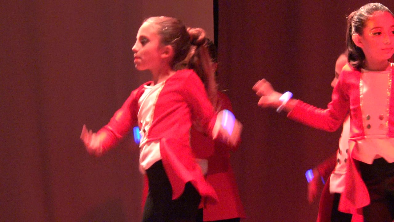 Two girls in red jackets moving their arms on stage.