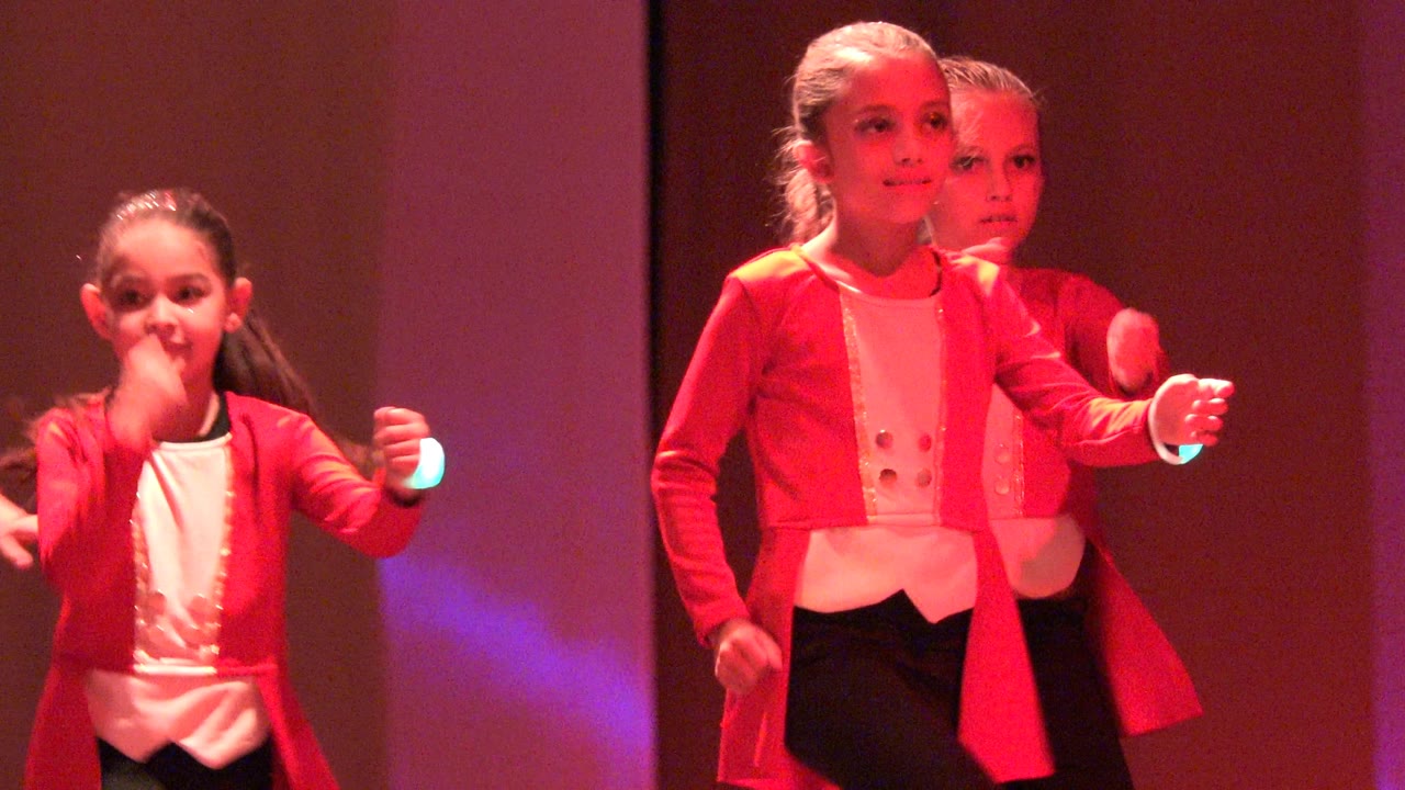 Child dancer steps forward with glowing wristbands on stage.