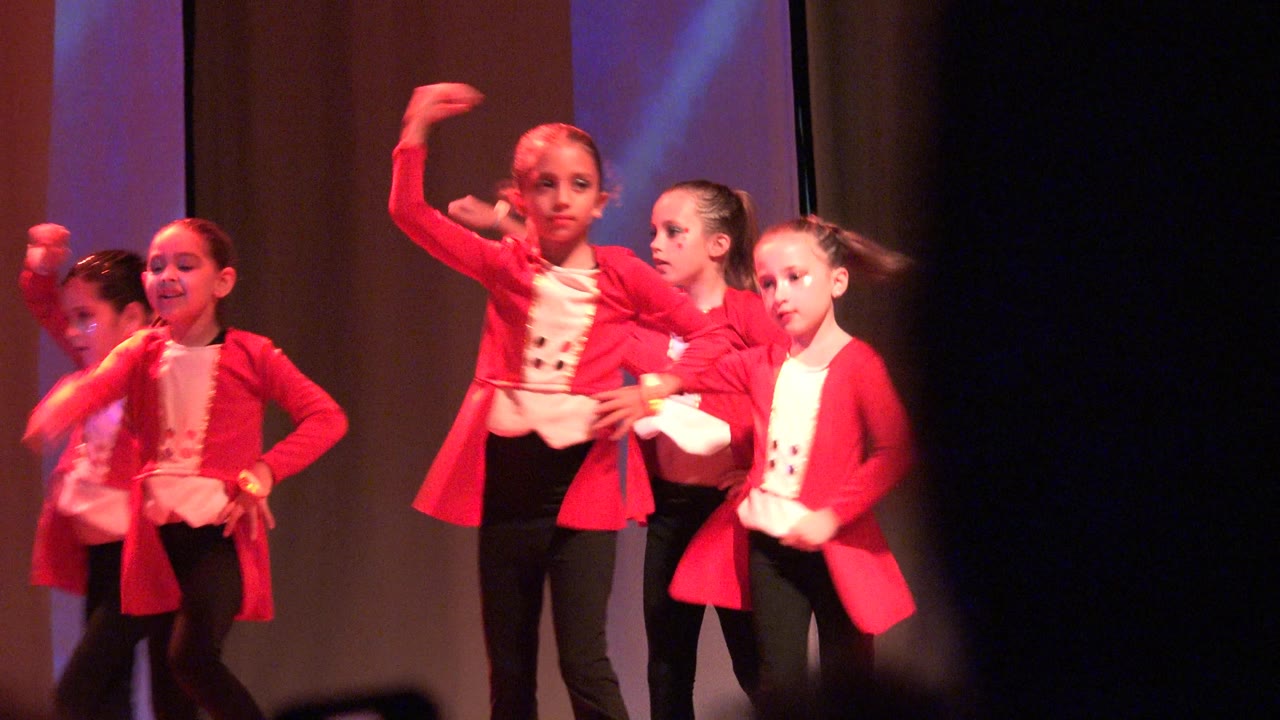 Young girls in red jackets and black pants dance on a stage in San Jose del Cabo BCS Mexico, with red lighting and dark curtains behind them.